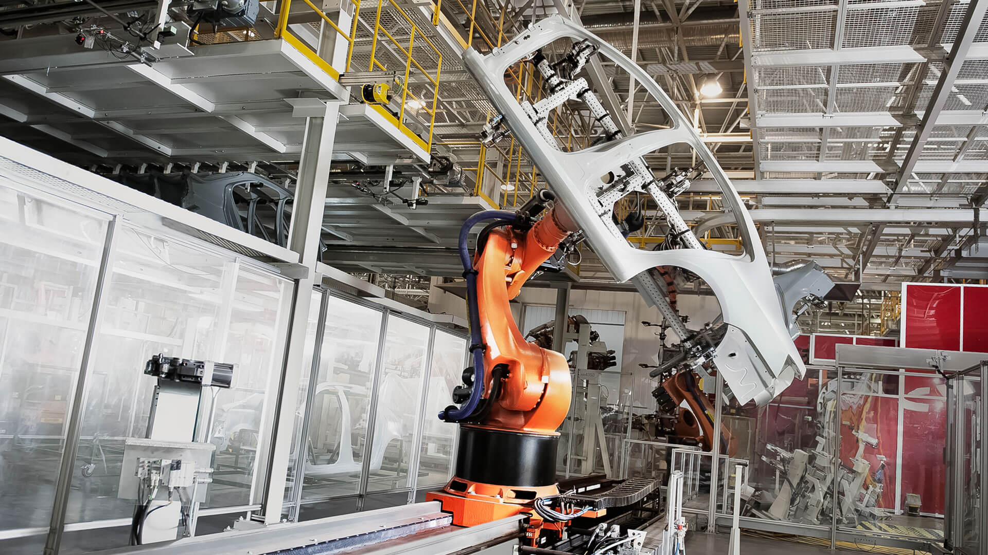 Ein Bild einer Industriehalle, in der Automobile produziert werden. Ein orangefarbener Schwenkarm bewegt gerade ein Autoteil.