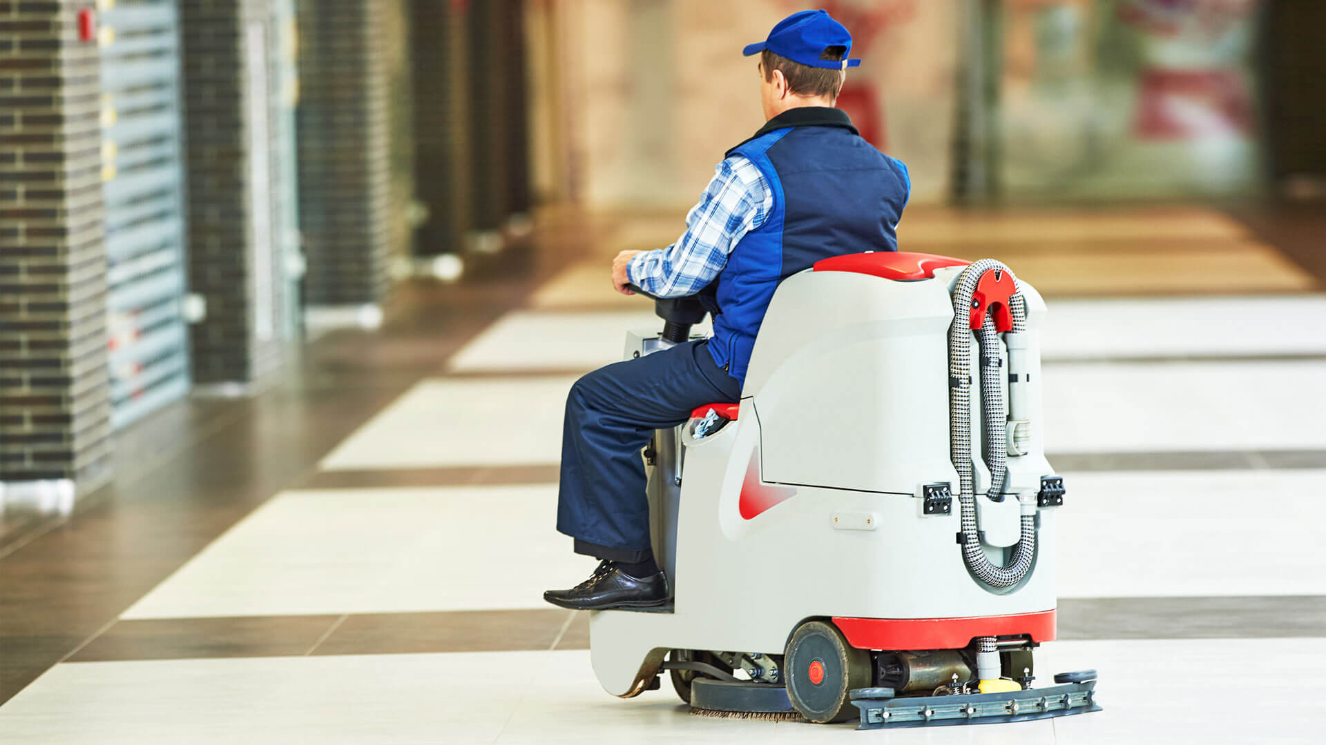 Ein Mann in blauer Kleidung sitzt in einem weiten Gang auf einer professionellen Scheuersaugmaschine zur Bodenreinigung.