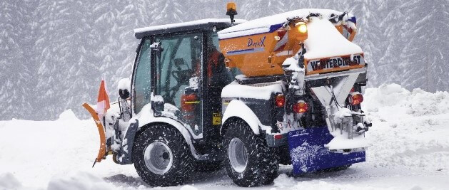 Im Schnee steht ein professionelles Räumfahrzeug, dass gerade einen Weg räumt, während es schneit.