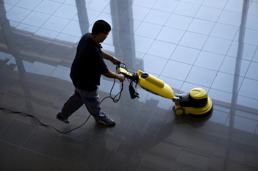 Ein Mann behandelt einen glänzenden Fliesenboden mit einem professionellen, gelben Reinigungsgerät.