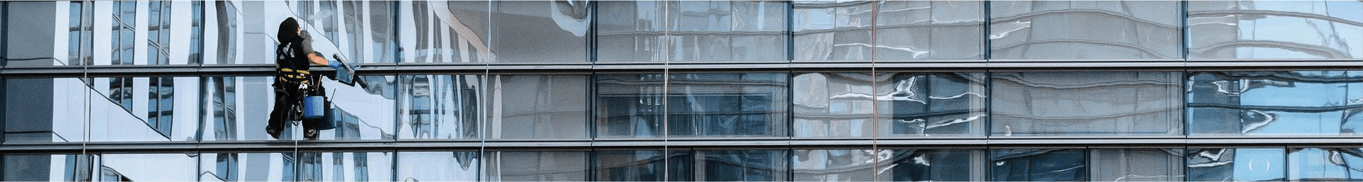 Ein Bild von der Glasfassade eines großen Firmengebäudes. Vor der Glasfassade ist eine ausgebildete Fachkraft zu sehen, die als Teil der Sonderreinigung die Fassade reinigt.